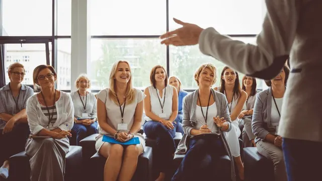 Grupo de profesionales sonríe mientras escucha a un ponente durante un taller.